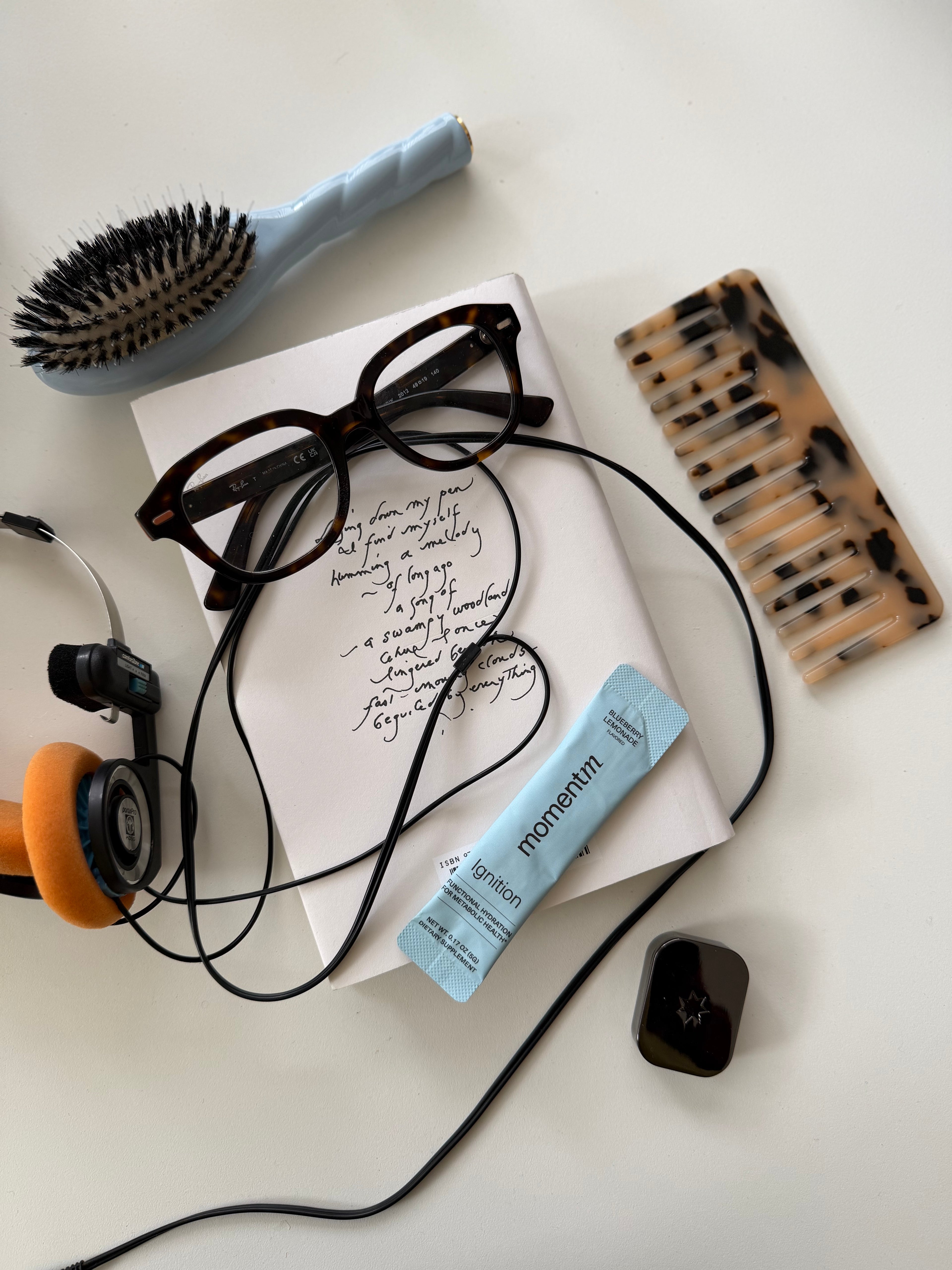 Hairbrush, comb, glasses, earphones, and a tube of lotion on a white surface.