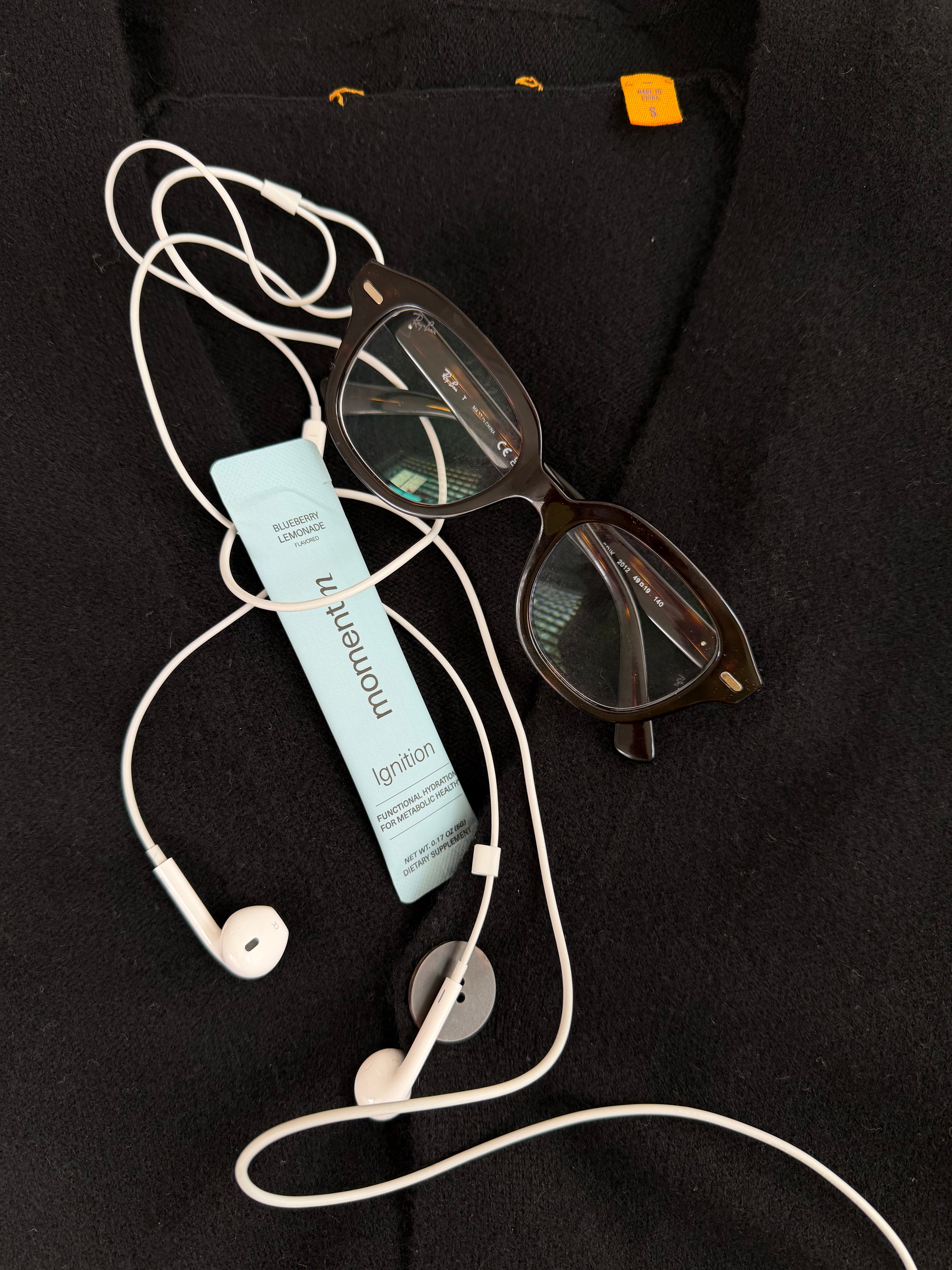 Pair of glasses, bottle of lotion, and earbuds on a black surface