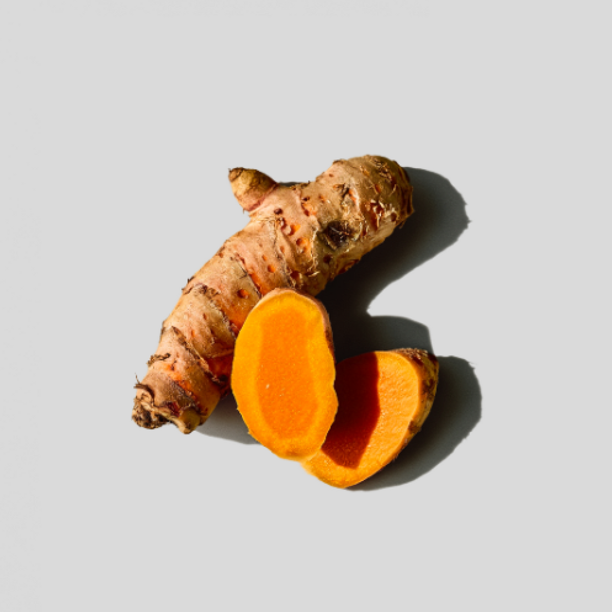 Turmeric root with a cut piece on a light gray background